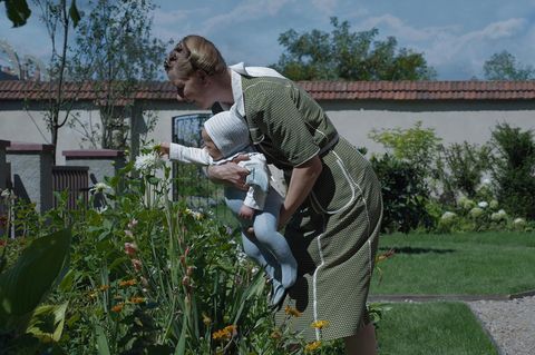 Sandra Hüller, wie sie mit einem Kleinkind im Arm Blumen betrachtet