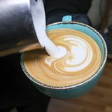 Milch wird in eine Tasse Kaffee gekippt