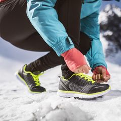 Unkenntliche Frau, die draußen in sonnigen Winterbergen joggt