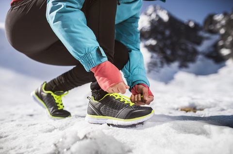 Unkenntliche Frau, die draußen in sonnigen Winterbergen joggt