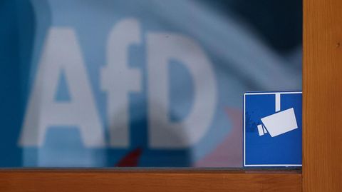 Das Piktogramm einer Überwachungskamera klebt auf einer Scheibe, in der sich das Logo der AfD spiegelt