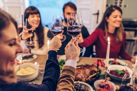Sodbrennen: Menschen stoßen mit Rotwein an einem gedeckten Tisch an