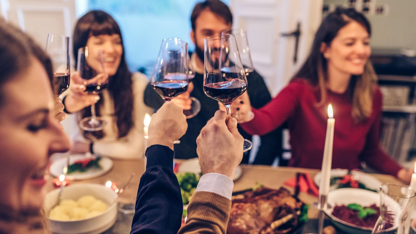 Sodbrennen: Menschen stoßen mit Rotwein an einem gedeckten Tisch an Sodbrennen: Menschen stoßen mit Rotwein an einem gedeckten Tisch an