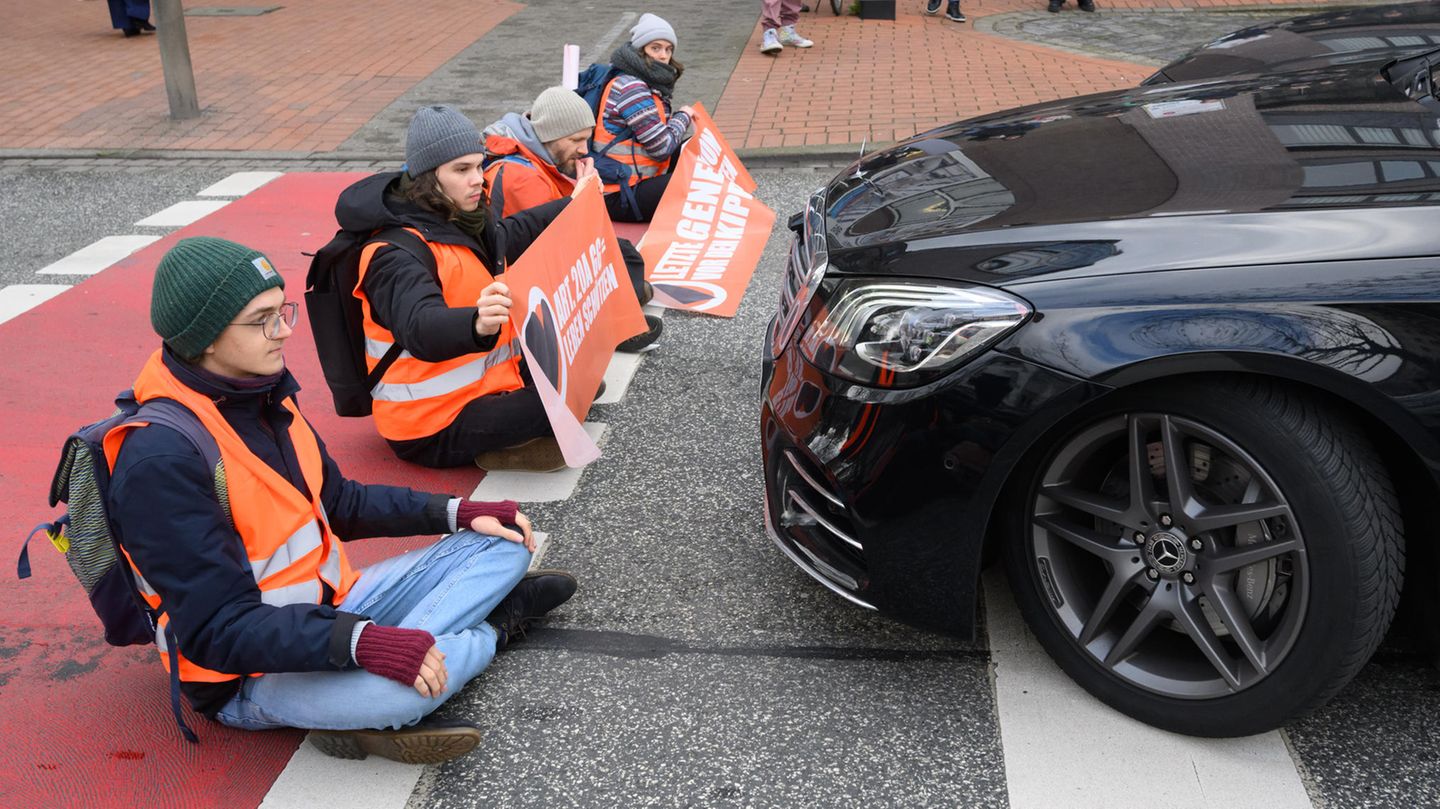 Demonstranten der Gruppe "Letzte Generation" blockieren eine Straße, vor ihnen steht ein schwarzer Mercedes