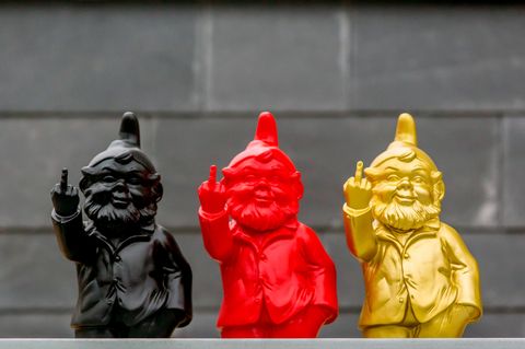 Drei Gartenzwerge in den Farben der Deutschlandfahne stehen nebeneinander und heben den Mittelfinger