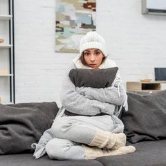 Junge Frau in warme Kleidung auf Couch sitzen und umarmt Kissen zu Hause