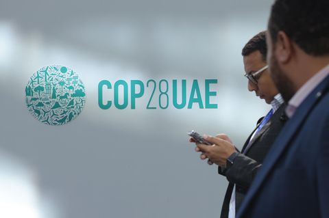 Zwei Männer in Anzügen laufen am Logo der Klimakonferenz COP28 in Dubai vorbei