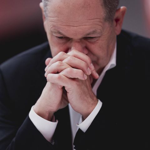 Kanzler Olaf Scholz trägt ein schwarzes Sakko, hat die Hände gefaltet und blickt nach unten.