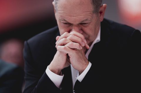 Kanzler Olaf Scholz trägt ein schwarzes Sakko, hat die Hände gefaltet und blickt nach unten.