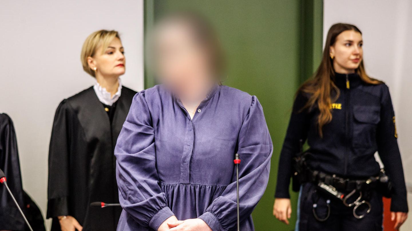 Die Angeklagte Andrea Tandler (m.) steht zu Prozessbeginn an ihrem Platz im Gerichtssaal