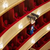 Eine Reinigungskraft in blauem Kittel reinigt das rote Plüsch der Sitze