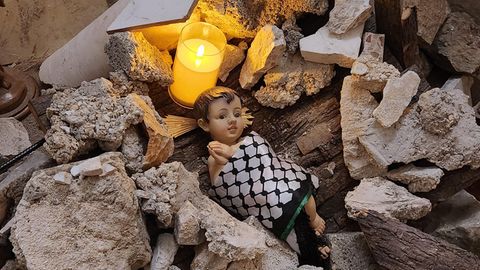 Eine Kinderholzfigur gewickelt in ein Palästinensertuch liegt in einer Kirche auf einem Haufen Steine.