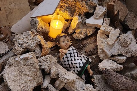 Eine Kinderholzfigur gewickelt in ein Palästinensertuch liegt in einer Kirche auf einem Haufen Steine.