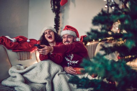 Weihnachtsfilme Disney Plus: Ein Paar sitzt auf der Couch und bedient freudestrahlend die Fernbedienung.