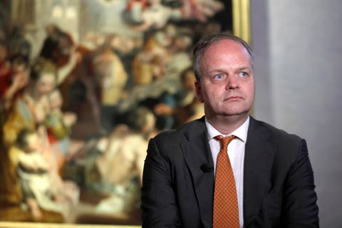 Eike Schmidt steht ernst vor einem Gemälde, das verschwommen im Hintergrund zu sehen ist
