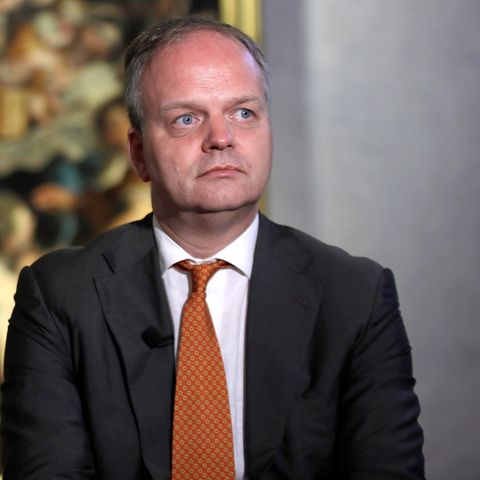 Eike Schmidt steht ernst vor einem Gemälde, das verschwommen im Hintergrund zu sehen ist