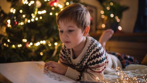 Ein Junge liest ein Buch am Weihnachtsbaum