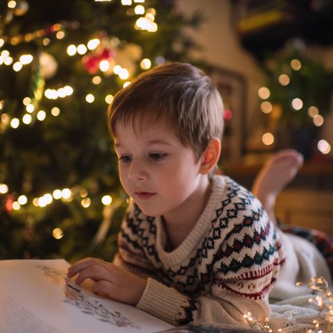 Ein Junge liest ein Buch am Weihnachtsbaum