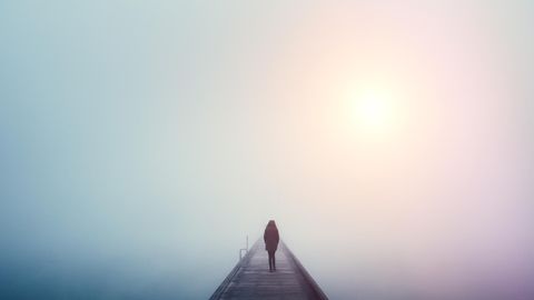 Eine Frau läuft in dichtem Nebel mit einer Winterjacke in Einsamkeit über einen Steg