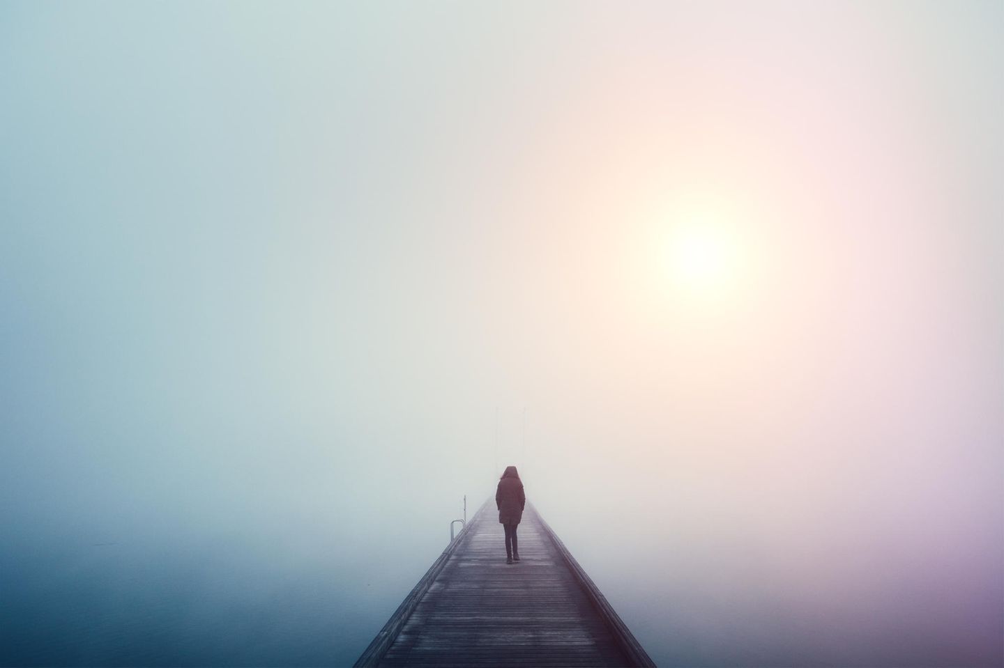 Eine Frau läuft in dichtem Nebel mit einer Winterjacke in Einsamkeit über einen Steg