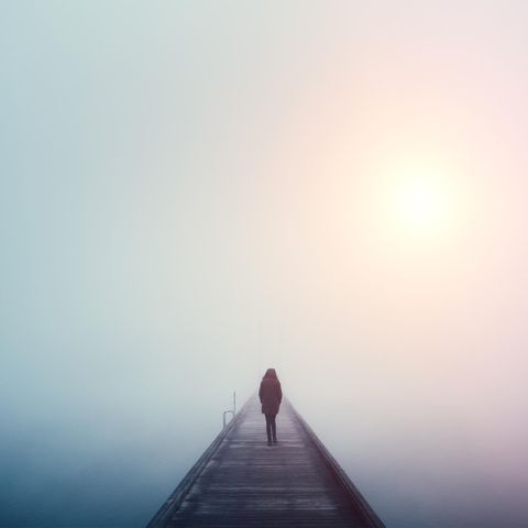 Einsamkeit Eine Frau läuft in dichtem Nebel mit einer Winterjacke in Einsamkeit über einen Steg