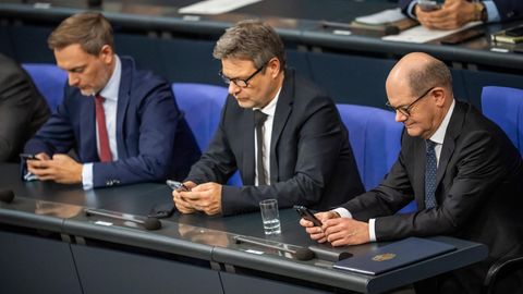 Olaf Scholz, Robert Habeck und Christian Lindner sitzen auf der Regierungsbank. Alle drei schauen auf ihr Handy.