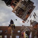 Ein Demonstrant sitzt auf einem Hochsitz neben einem Gebäude das gerade von einem Bagger abgerissen wird