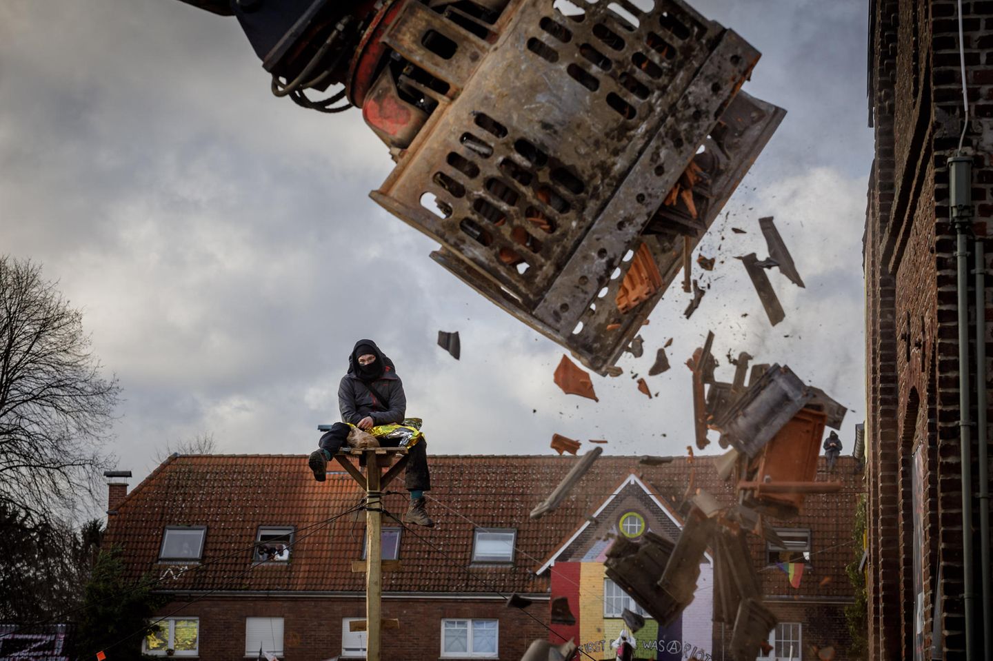 Ein Demonstrant sitzt auf einem Hochsitz neben einem Gebäude das gerade von einem Bagger abgerissen wird