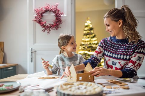 Eine Mutter schmückt mit ihrer Tochter ein Lebkuchenhaus