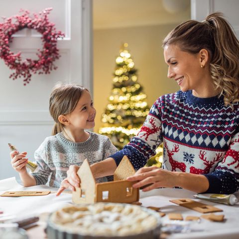 Eine Mutter schmückt mit ihrer Tochter ein Lebkuchenhaus