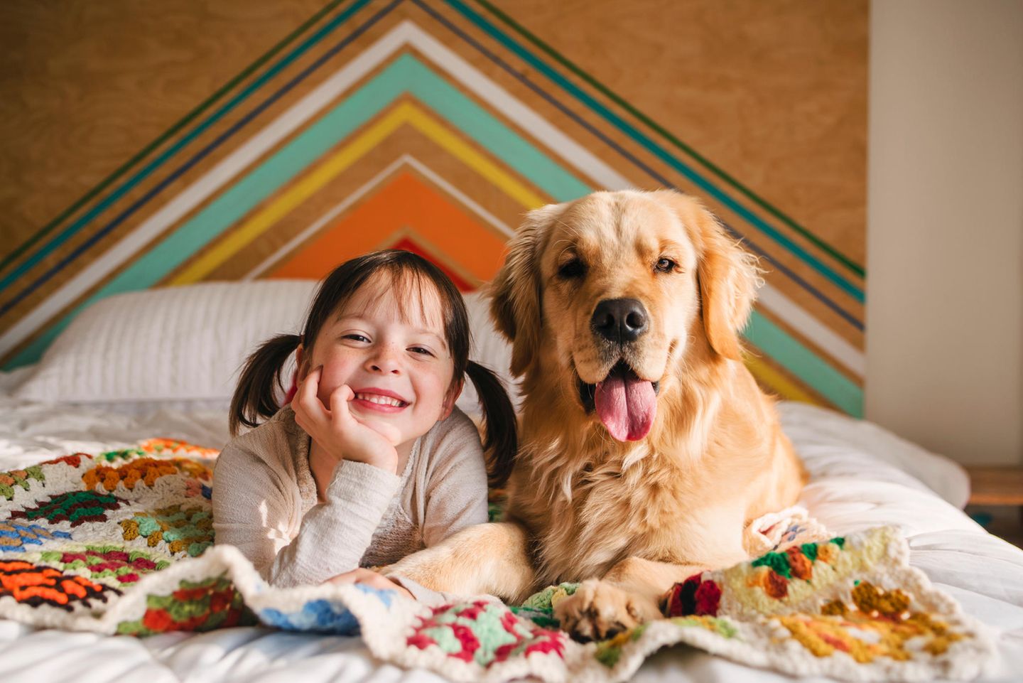 Ein Mädchen liegt mit einem Golden Retriever auf dem Bett