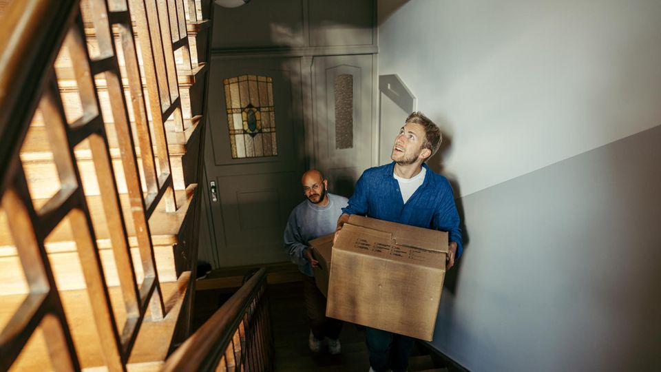 Ein Mann trägt einen Umzugskarton durch ein Treppenhaus