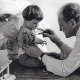 Nebenwirkungen  Ist dies ein guter, hoffnungsvoller Tag? Oder wieder ein Tag, an dem das Kind schmerzlich spürt, dass es anders ist als die anderen? Ein Arzt und eine Schwester passen dem Mädchen in einem spezialisierten Kinderheim in Neuwied eine Arm-prothese an. Fehlbildungen an Armen und Beinen gehören zu den schweren Schädigungen, die der Wirkstoff Thalidomid hervorgerufen hatte – enthalten im Schlaf- und Beruhigungsmittel Contergan. Das anfangs als „gut verträglich“ bezeichnete Medikament, das seit 1957 rezeptfrei erhältlich ist, war nicht an Schwangeren getestet worden. Aber schon eine einzige Tablette genügt, um dem heranwachsenden Kind im Mutterleib schwer zu schaden. Allein in Deutschland kommen so etwa 5000 Kinder mit Missbildungen zur Welt. 40 Prozent von ihnen sterben kurz nach der Geburt oder im Säuglingsalter. Ein Prozess gegen die Herstellerfirma Grünenthal wird 1970 eingestellt. Die Opfer des Skandals erhalten Entschädigungszahlungen aus einem Stiftungsfonds, der von Grünenthal und dem Bund bestückt wird. 1997 ist das Geld aufgebraucht. Seitdem zahlt der Bund die Contergan-Renten weitgehend allein.