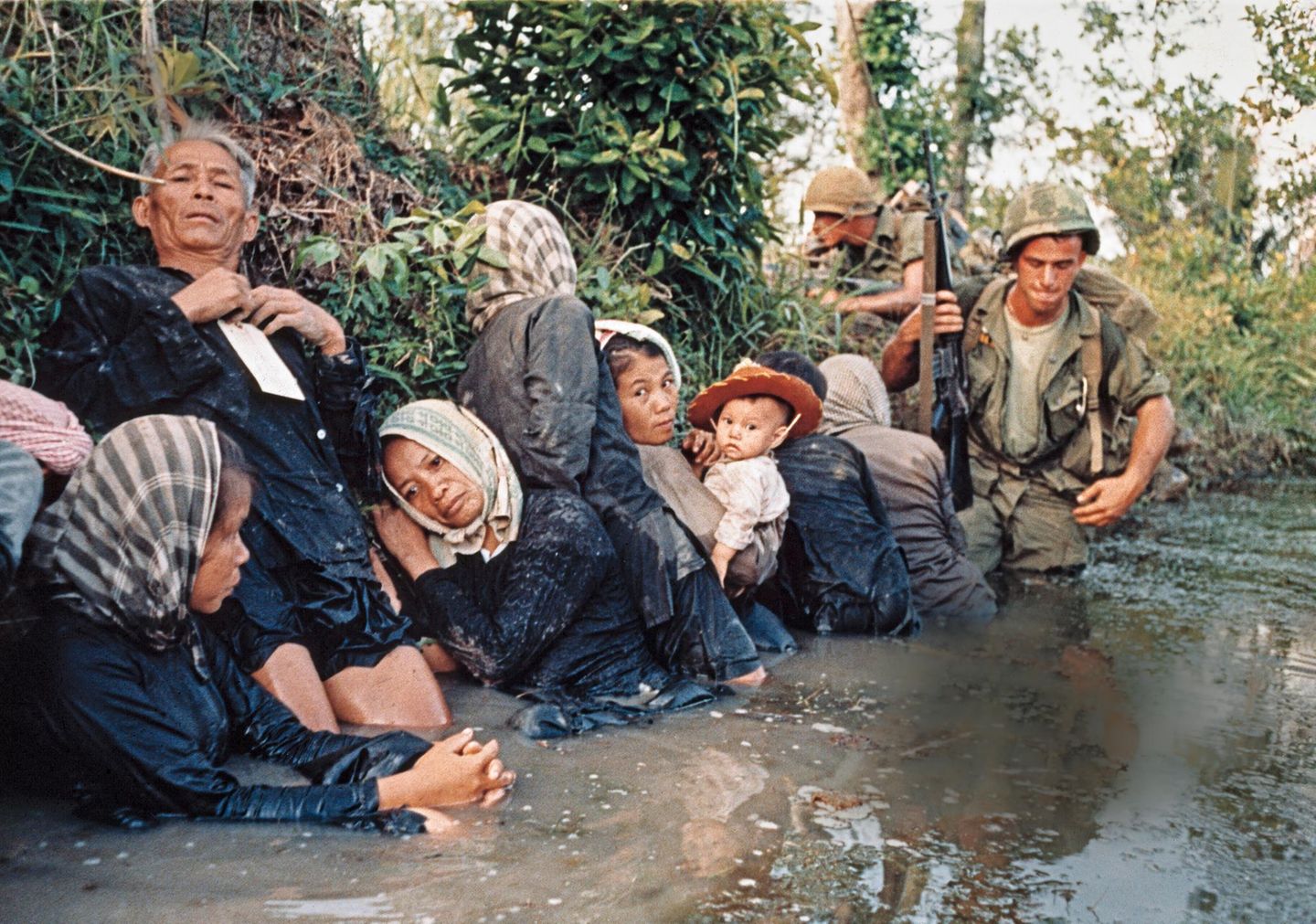 1966 - Vietnam Dschungelkrieg In den Gesichtern der Frauen stehen Leere und Verzweiflung. Sie kauern in einem schlammigen Kanal in Bao Trai westlich von Saigon und versuchen den Krieg zu ertragen: Es sind südvietnamesische Zivilisten, die hier vor dem Feuer der Vietcong in Deckung gehen. Fallschirmjäger der 173. US-Luftlandebrigade eskortieren sie während eines US-Angriffs durch schwere Gefechte. Die Amerikaner rüsten in diesem Jahr noch einmal auf: Sie sind mit 385 000 Soldaten in Vietnam, doch ohne entscheidende Erfolge zu erzielen. In den USA formiert sich eine Protestbewegung gegen die Beteiligung am Vietnamkrieg, doch erst im März 1973 verlassen die letzten amerikanischen Truppen das Land.