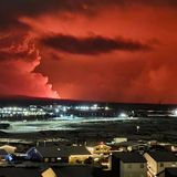 Häuser in der Ortschaft Hafnarfjörður sind zu sehen, während in der Ferne Rauch aufsteigt