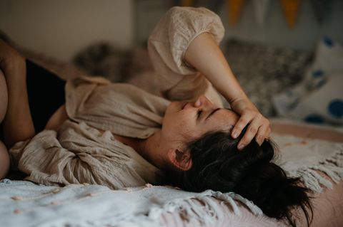 Eine Frau hält sich verzweifelt die Hand auf die Stirn während sie im Bett liegt