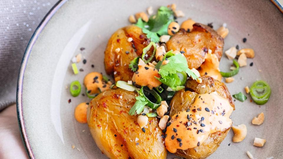 SMASHED POTATOES  Mit Kokostandoorimarinade & Erdnusskernen  Dieses Rezept ist eine ideale Resteverwertung für übrig gebliebene Pellkartoffeln. Sie werden mit dem Handballen etwas platt­ bzw. angedrückt, dann mit der Tandoori-­Mari­nade bestrichen und im heißen Ofen kross gebacken. Dazu gibt’s einen schnell gemixten Würz­-Schmand, Koriander und knackige Erdnusskerne.  Zutaten für 4 Portionen:  Für die Smashed Potatoes  1 kg kleine Drillings-Kartoffeln (mit Schale gekocht)  Für die Marinade  125 ml Kokosmilch, 2 geh. TL Tandoori-Paste, 1 EL Ahornsirup, 1 Spritzer Limettensaft Salz  Für den Dip  150 g Schmand oder Crème fraîche (alternativ Kokosjoghurt), 1TL Tandoori-Paste, 1⁄2 TL Ahornsirup, 1 großer Spritzer Limettensaft, Salz  Außerdem: 4 EL Korianderblätter (alternativ Petersilie), 4 EL geröstete und gesalzene Erdnusskerne     Zubereitung:  Den Backofen auf 185 °C (Umluft) vorheizen.  Für die Smashed Potatoes die Kartoffeln auf ein mit Backpapier ausgelegtes Blech setzen und jeweils mit dem Handballen leicht platt drücken, sodass die Kartoffeln die Marinade besser aufnehmen.  Für die Marinade Kokosmilch, Tandoori-Paste, Ahornsirup, Limettensaft und Salz mixen und abschmecken. Gleichmäßig über die platt gedrückten Kartoffeln gießen. Im heißen Ofen rund 30 Minuten knusprig backen.  Während der Backzeit aus Schmand, Tandoori-Paste, Ahornsirup, Limettensaft und Salz einen würzigen Dip mixen und abschmecken. Die Erdnusskerne hacken.  Die heißen Kartoffeln mit dem Dip, den Korianderblättern und den knackigen Erdnusskernen servieren.