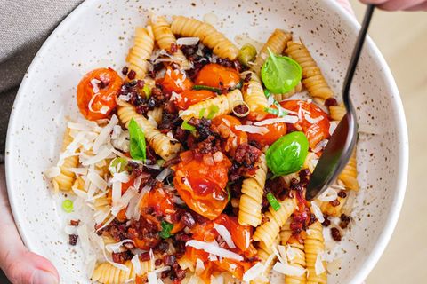 OFENTOMATEN-PASTA  mit Parmesan & karamellisierten Speck  Diese Ofentomaten­-Pasta gehört zu meinen liebsten Soulfood­-Gerichten überhaupt! Ob einfach schnell nach Feierabend oder auch als besonderes Pastagericht für Gäste – die Kombination aus den gerösteten Ofentomaten, dem karamellisierten Speck sowie frisch gehobeltem Parmesan und frischen Basilikumblättern ist ein absoluter Treffer.  Zutaten für 4 Portionen  Für die Pasta: 500 g Fusilli, Salz, Ofentomaten  Für den karamellisierten Speck: 125 g geräucherte Schinkenspeck- Würfel, 1 TL Ahornsirup  Außerdem: 4 EL frisch gehobelter oder geraspelter Parmesan, 4 EL Basilikumblätter     Zubereitung:  Für die Pasta die Fusilli in kochendem Salzwasser in einem großen Topf nicht ganz al dente kochen, das heißt, bereits 1 Minute vor Ende der Garzeit abgießen. Die Ofentomaten nach Rezept zubereiten und nun weiterverarbeiten: die Fusilli abgießen, dabei eine kleine Tasse stärkehaltiges Nudelwasser aufbewahren. Die Fusilli wieder in den großen Topf geben, mit den Ofentomaten samt Sud erwärmen und kurz fertig köcheln. So verbinden sich Nudeln und Sauce optimal.  Für den karamellisierten Speck die Schinkenwürfel in einer beschichteten Pfanne ohne zusätzliches Fett auslassen und 10–15 Minuten rundherum bei mittlerer Hitze braten. Dann den Ahornsirup zugeben, untermengen und die Schinkenwürfel kurz karamellisieren lassen.  Den karamellisierten Speck unter die Nudeln heben und die Pasta in Schalen oder tiefen Tellern anrichten. Mit frisch gehobeltem Parmesan und Basilikumblättern angerichtet servieren.