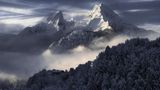 Alpen-Gebirge türmt sich hinter einem verschneiten Wald auf