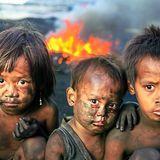 Drei mit Ruß verschmierte Kinder asiatischer Abstammung schauen in die Kamera, hinter ihnen eine Flamme
