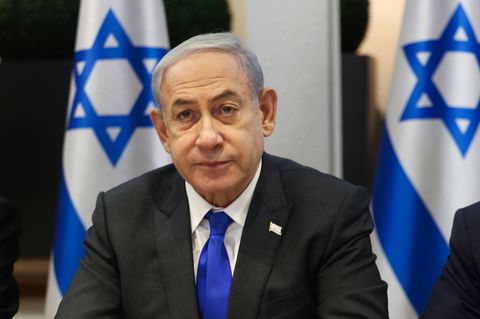 Premier Benjamin Netanjahu sitzt vor mehreren Flaggen von Israel