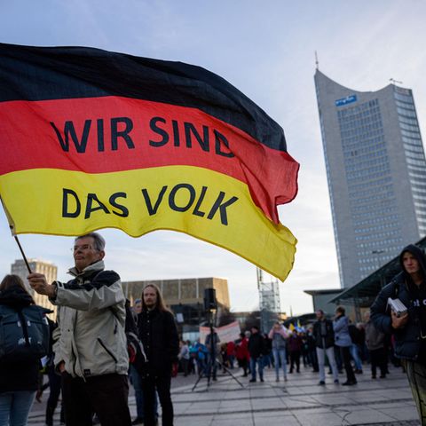 “Wir sind das Volk” steht auf einer riesigen Deutschland Flagge die ein älterer Mann bei einer Querdenkerdemonstration 2021 in Leipzig schwingt. Dieses durch solche Parolen vermittelte Zugehörigkeitsgefühl, kann sehr attraktiv auf einsame Menschen wirken 