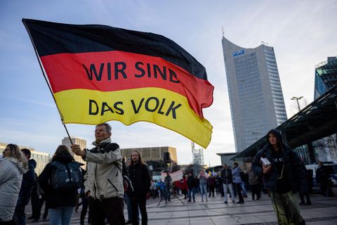 “Wir sind das Volk” steht auf einer riesigen Deutschland Flagge die ein älterer Mann bei einer Querdenkerdemonstration 2021 in Leipzig schwingt. Dieses durch solche Parolen vermittelte Zugehörigkeitsgefühl, kann sehr attraktiv auf einsame Menschen wirken 