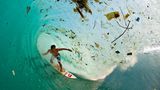 Der Surfer erwischt eine Welle, die sehr viel Müll mit sich trägt.