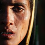 Eine dunkelhaarige Frau schaut in die Kamera. Eine Träne ist ihr Gesicht herunter gelaufen.