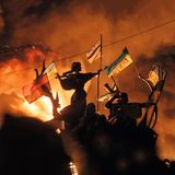 Proteste im dunkeln. Fahnen wehen im Wind während diese vom Feuer von hinten beleuchtet werden.