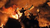 Proteste im dunkeln. Fahnen wehen im Wind während diese vom Feuer von hinten beleuchtet werden.