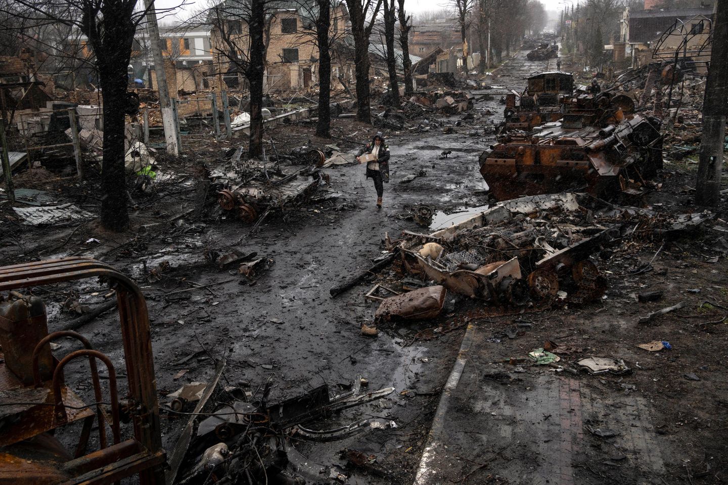 2022 – Ukraine Eine zerstörte und dunkle, matschige Straße wird von einer Person mit Parker durchqueert.
