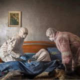 Das Schlafzimmer der älteren Frau während Helfer in Schutzanzügen sich vorbereiten um sie aus dem Bett zu heben.