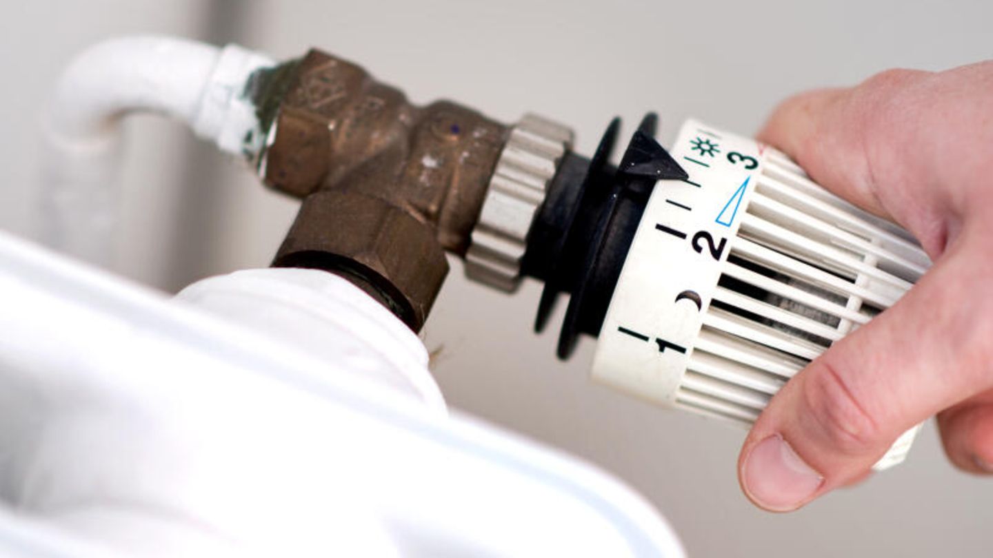 Eine Frau dreht am Thermostat einer Heizung